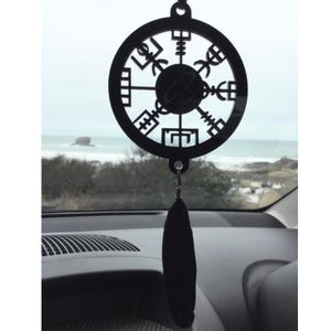 May include: Black car charm with a black and white compass design. The charm is hanging from the rearview mirror of a car. The compass design features a circle with eight points and a central star.