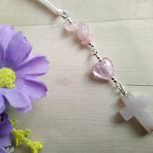 May include: A pink rear view mirror charm, with genuine rose quartz chip beads leading down to a pink foil glass heart and a rose quartz cross on the end.