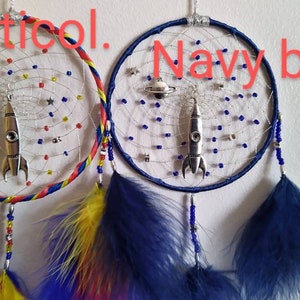 Pu&ograve; includere: Due acchiappasogni con un ciondolo a forma di razzo e pianeta che pendono da essi. Un acchiappasogni ha un anello esterno blu, rosso e giallo, l'altro ha un anello esterno blu navy. Entrambi gli acchiappasogni hanno piume blu e bianche.