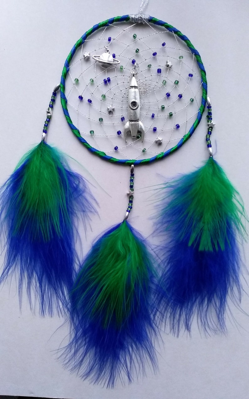 Pu&ograve; includere: Un acchiappasogni blu e verde con un ciondolo a forma di razzo e pianeta argentato. L'acchiappasogni ha tre piume blu e verdi che pendono.