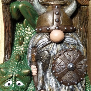 K&ouml;nnte beinhalten: Detaillierte Figur eines Wikinger-Zwergs und eines Drachen. Der Zwerg tr&auml;gt einen geh&ouml;rnten Helm, hat einen langen wei&szlig;en Bart und h&auml;lt eine Axt und einen Schild. Der gr&uuml;ne Drache hat einen traurigen Gesichtsausdruck.