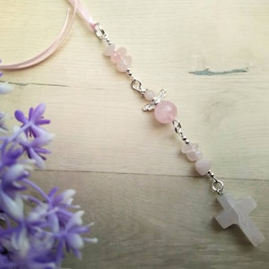 Puede incluir: Un brazalete de charms rosa y plateado con un charm de cruz, un charm de &aacute;ngel y cuentas rosas.