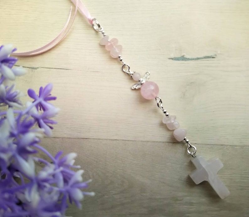 Puede incluir: Un brazalete de charms rosa y plateado con un charm de cruz, un charm de &aacute;ngel y cuentas rosas.