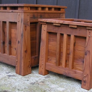 May include: Two wooden planter boxes, one on top of the other, with a dark brown stain. The boxes have a slatted design and are made of solid wood.