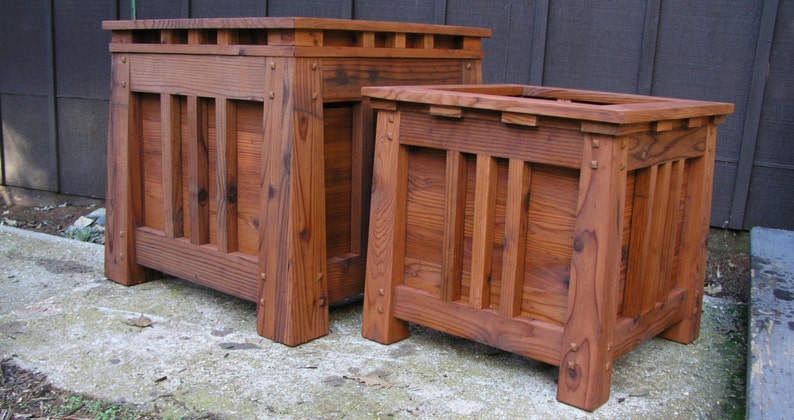 May include: Two wooden planter boxes, one on top of the other, with a dark brown stain. The boxes have a slatted design and are made of solid wood.