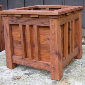 May include: A large, rectangular wooden planter box with a dark reddish-brown stain. The planter has a simple, traditional design with vertical slats and a raised lip around the top.