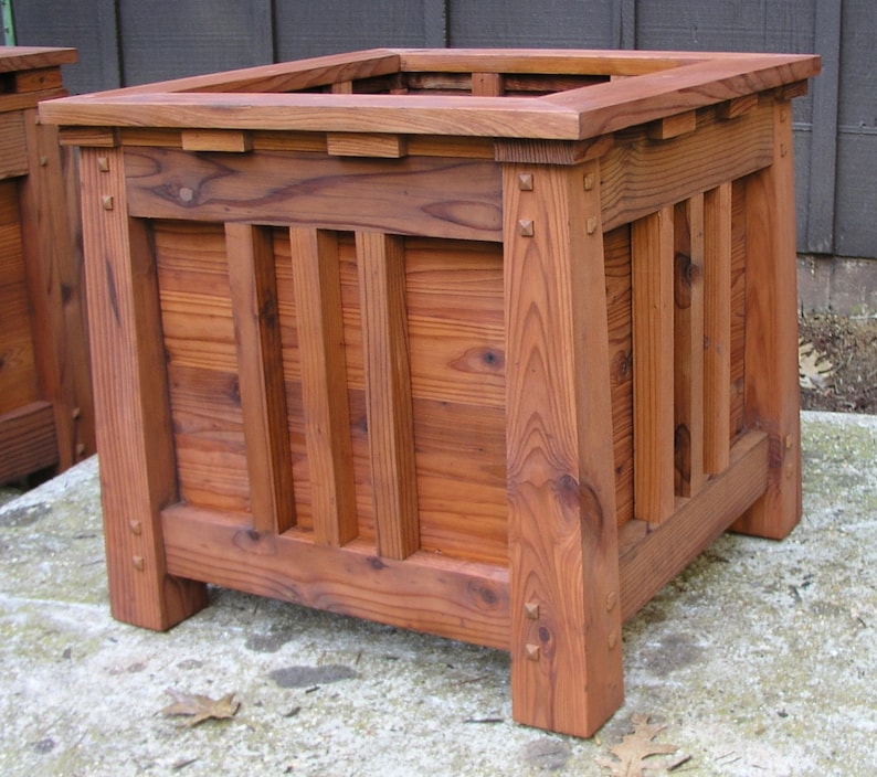 May include: A large, rectangular wooden planter box with a dark reddish-brown stain. The planter has a simple, traditional design with vertical slats and a raised lip around the top.
