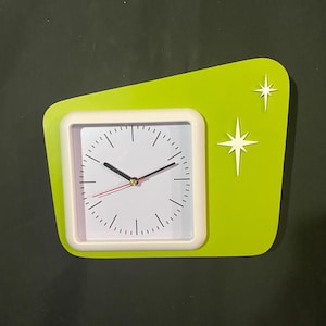 May include: A retro-style clock with a white face, black hands, and a red second hand. The clock is set in a square white frame, mounted on a lime green, asymmetrical background with two white starburst accents.