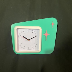 May include: A retro-style wall clock with a square white clock face and a mint green background. The clock has a white frame and pink starburst accents. The clock hands are black with a red second hand.