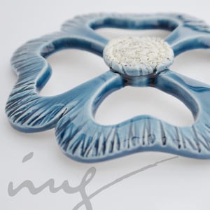 May include: A blue ceramic flower with a white centre. The flower has a textured surface and is shaped like a four-leaf clover.