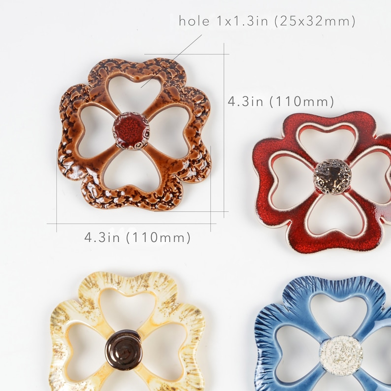 May include: Four ceramic flower-shaped pot holders in different colours: brown with red centre, red with gold centre, yellow with brown centre, and blue with white centre. Each pot holder measures 11 cm in diameter and has a 2.5x3.2 cm hole in the centre.