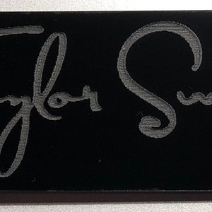 May include: Black keychain with a silver key ring and the engraved text "Taylor Swift" in a cursive font.