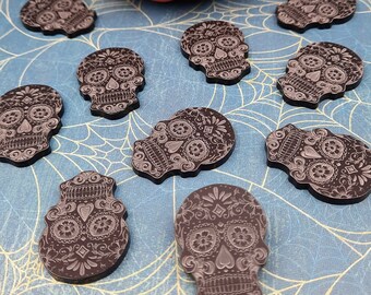 Könnte beinhalten: Neun schwarze Zucker Schädel Charms mit komplizierten floralen Designs. Die Charms sind auf einem blauen Hintergrund mit einem Spinnennetz Muster angeordnet.