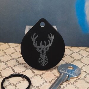 May include: Black metal key chain with a geometric deer design. The key chain is attached to a silver key.