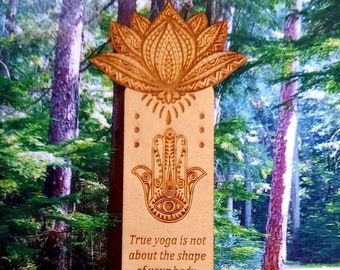 May include: Wooden bookmark with a lotus flower design, a hamsa hand, and a quote about yoga. The quote reads: "True yoga is not about the shape of your body, but the shape of your life."