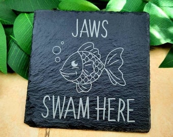 May include: Black slate coaster with a white outline of a fish and the text "JAWS SWAM HERE".