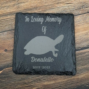 Könnte beinhalten: Schwarze Schiefer-Gedenktafel mit dem Text "In Loving Memory Of Donatello 2011-2021" und einer Silhouette einer Schildkröte.