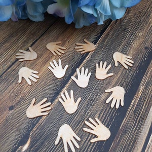 Könnte beinhalten: Eine Sammlung von ausgeschnittenen Holzhandflächen auf einer braunen Holzoberfläche. Die Handformen sind alle nach oben gerichtet und in einem Kreis angeordnet.