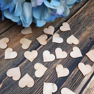 May include: A scattering of natural wood heart shapes on a dark wood surface. The hearts are all the same size and shape, and they are arranged in a random pattern.