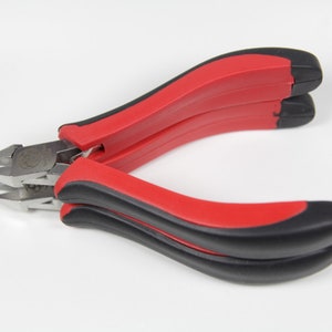 May include: A pair of diagonal cutting pliers with red and black handles. The metal cutting edges are silver and angled. The pliers are open, ready for use, against a white background.