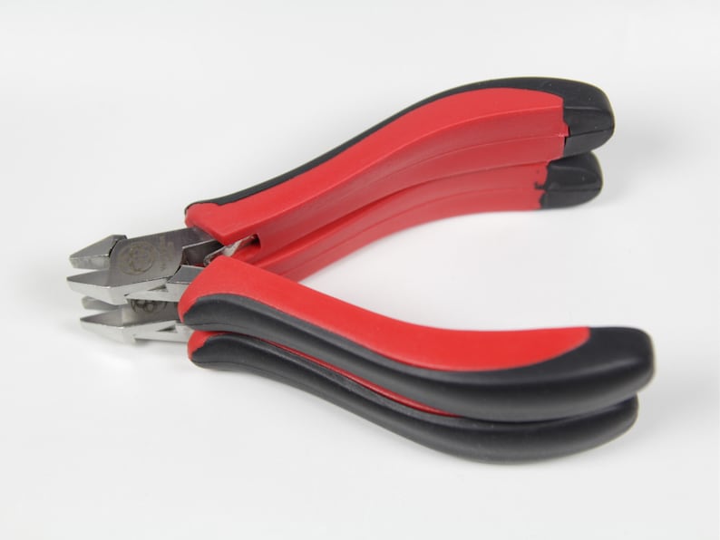 May include: A pair of diagonal cutting pliers with red and black handles. The metal cutting edges are silver and angled. The pliers are open, ready for use, against a white background.