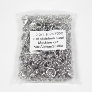 Könnte beinhalten: Ein klarer Plastikbeutel gefüllt mit zahlreichen kleinen, glänzenden, silberfarbenen Metallringen. Ein weißes Etikett auf dem Beutel lautet "12.0x1.8mm #352 316 stainless steel Machine cut VanAlphenStudio". Die Ringe sind aus Edelstahl.