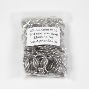 以下が含まれることがあります： 銀色の金属製のキーリングが詰まった透明なビニール袋。袋には「20.0x2.0mm #169 304ステンレススチール 機械切断 VanAlphenStudio」と書かれたラベルが付いています。