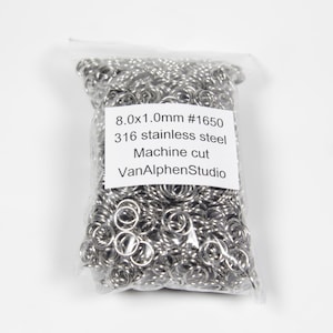 Op de afbeelding: Een doorzichtige plastic zak gevuld met zilveren springringen. De zak heeft een wit label met de tekst "8.0x1.0mm #1650 316 roestvrij staal Machine gesneden VanAlphenStudio".