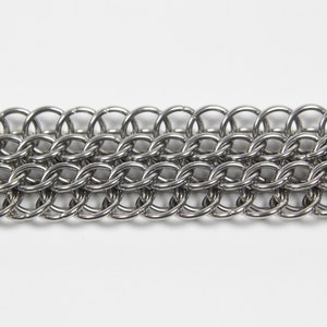 May include: Close-up of a section of chainmail. The chainmail is made of small, interlocking, silver-colored metal rings. The rings are arranged in rows and columns, creating a flexible, textured surface. The background is plain white.