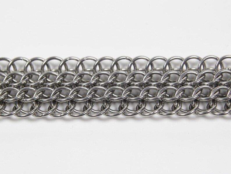 May include: Close-up of a section of chainmail. The chainmail is made of small, interlocking, silver-colored metal rings. The rings are arranged in rows and columns, creating a flexible, textured surface. The background is plain white.