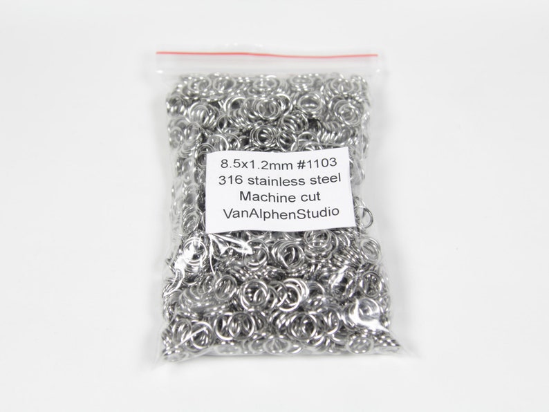 May include: A clear plastic bag filled with silver jump rings. The bag has a label that reads "8.5x1.2mm #1103 316 stainless steel Machine cut VanAlphenStudio".