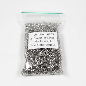 May include: A transparent plastic bag containing many small, silver metal rings. The bag is sealed with a green strip. A white label displays text: "8.0x1.4mm #935 316 stainless steel Machine cut VanAlphenStudio."