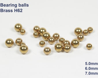 May include: A collection of brass bearing balls in various sizes, including 5.0mm, 6.0mm, and 7.0mm. The balls are a shiny gold color and are scattered on a white surface.