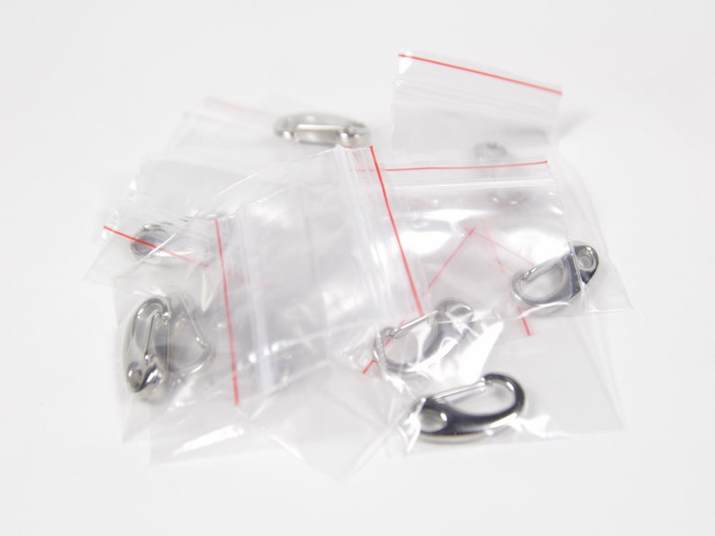 May include: A close-up of several small silver metal clasps in clear plastic bags. The bags have red lines along the edges.