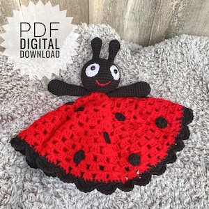 Op de afbeelding: Een gehaakte lieveheersbeestje babydeken met een zwart en rood ontwerp. De deken heeft een klein lieveheersbeestje amigurumi speelgoed met zwarte ogen en een glimlachende mond.