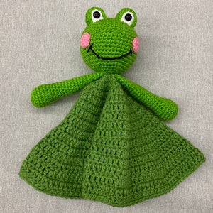 Puede incluir: Manta de beb&eacute; de ganchillo verde en forma de rana con mejillas rosas y ojos negros. La manta est&aacute; hecha con un patr&oacute;n de punto sencillo y tiene una textura suave y acogedora.