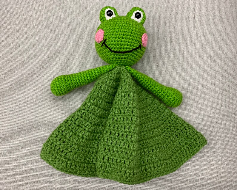 Puede incluir: Manta de beb&eacute; de ganchillo verde en forma de rana con mejillas rosas y ojos negros. La manta est&aacute; hecha con un patr&oacute;n de punto sencillo y tiene una textura suave y acogedora.