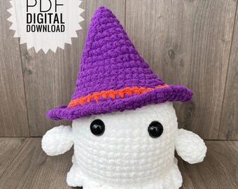 Puede incluir: Un fantasma blanco de crochet que lleva un sombrero de bruja morado y naranja. El fantasma tiene dos ojos negros y una pequeña boca.