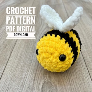 May include: A crocheted bee toy with yellow and black stripes, black eyes, and white wings. The image includes the text "CROCHET PATTERN PDF DIGITAL DOWNLOAD". The bee is a handmade item.