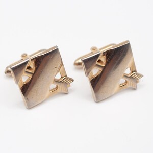 May include: A set of gold-toned cufflinks and a tie clip. The cufflinks and tie clip feature a geometric design with an arrow motif.