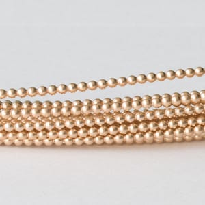 May include: A close-up of a strand of gold-coloured beads. The beads are small and round, and they are strung together in a long, continuous strand.