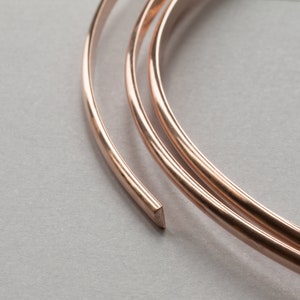 May include: Three spools of rose gold colored wire, coiled and overlapping on a white surface.