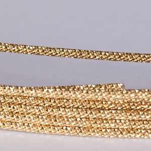 Peut inclure: Gros plan d'un cordon métallique doré, enroulé en spirale. Le cordon a une surface texturée et une finition brillante.