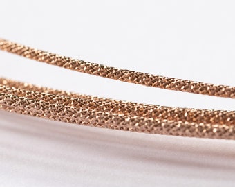 May include: Close-up of two strands of rose gold wire with a textured surface.