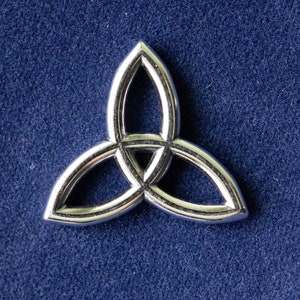 Può includere: Un ciondolo in metallo color argento a forma di nodo triquetra, un simbolo celtico di unità ed eternità. Il ciondolo è su uno sfondo blu.