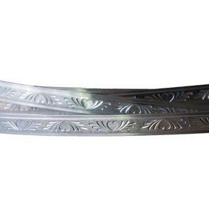 May include: Close-up of silver metal trim with a decorative heart and floral pattern.