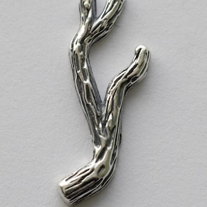 May include: A silver charm in the shape of a tree branch with a textured surface.