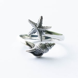 May include: A silver ring featuring a starfish and seashell design. The ring is adjustable and can be worn on any finger.