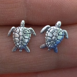 May include: A pair of silver turtle earrings. The turtles are facing forward with their heads up and their legs outstretched. The earrings are small and delicate.