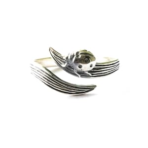 May include: A silver-toned ring featuring a detailed ladybug design. The ring wraps around the finger with a textured, leaf-like band. The ladybug has a rounded body with small, dark spots.